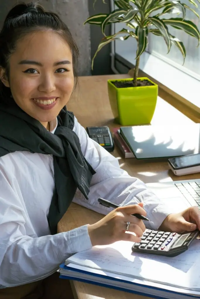 Confident woman working with calculator in bright office setting, surrounded by office tools.